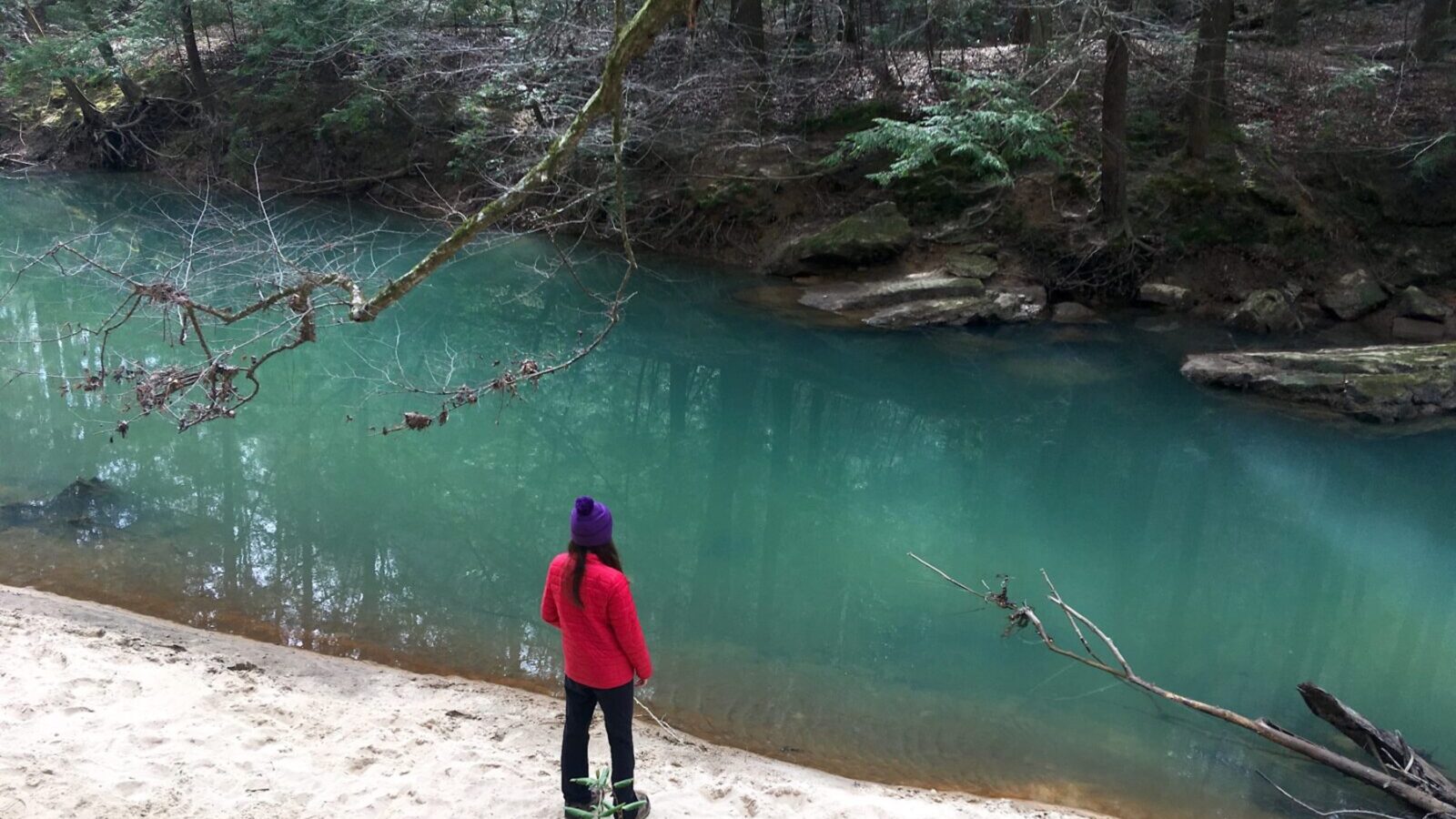 A woman stands by blue water on a trail