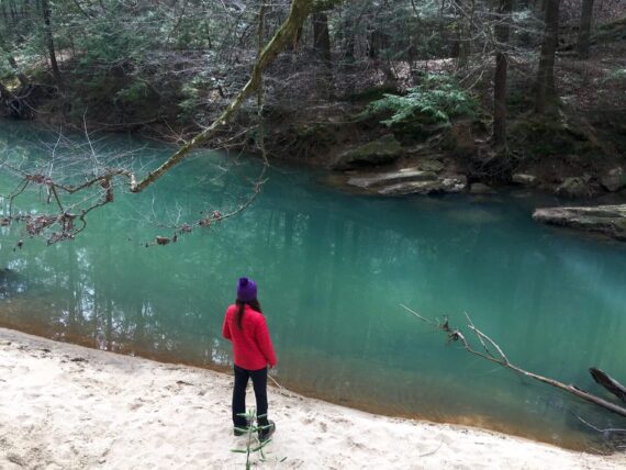 A woman stands by blue water on a trail