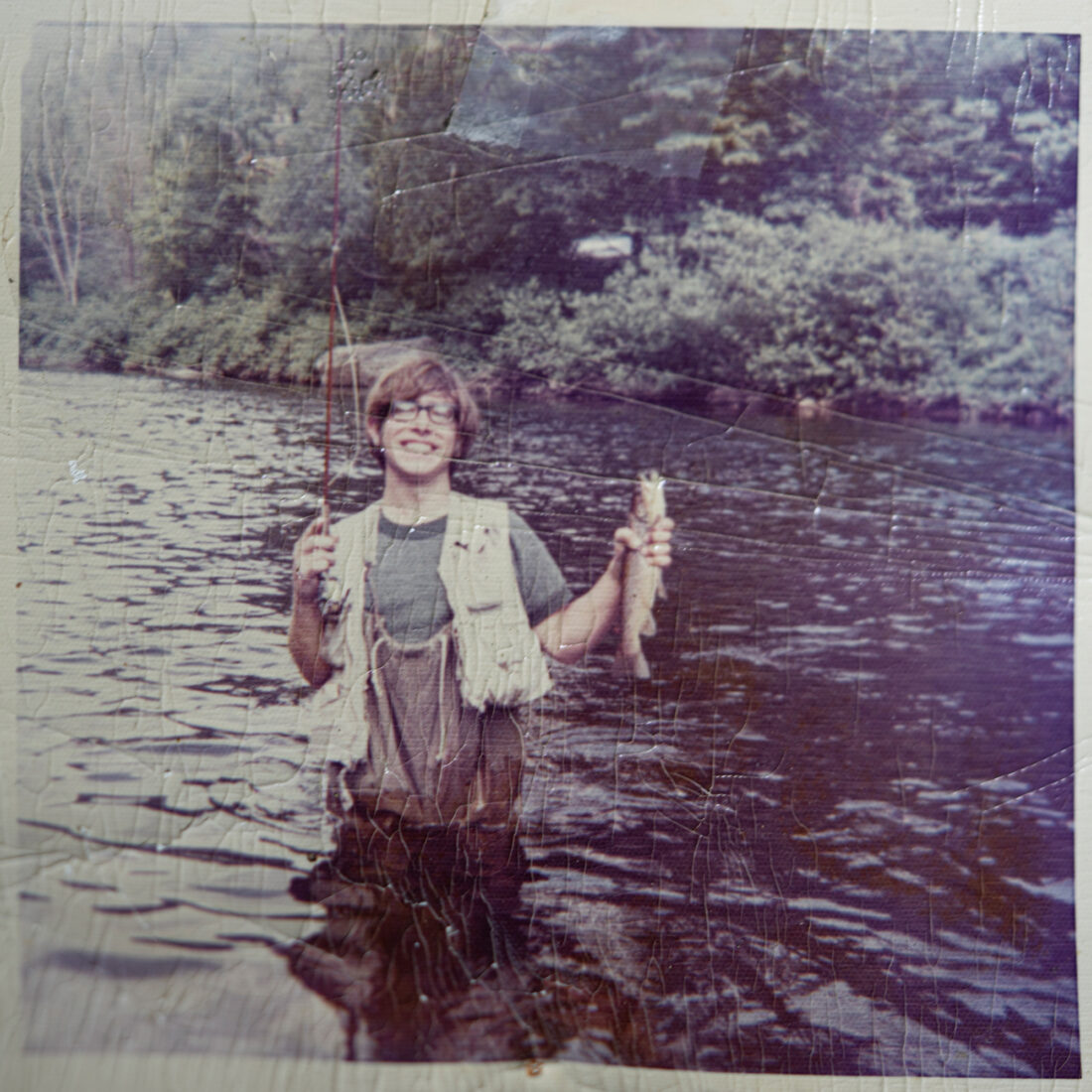 An old photo of a young man holding a fish while standing in the river