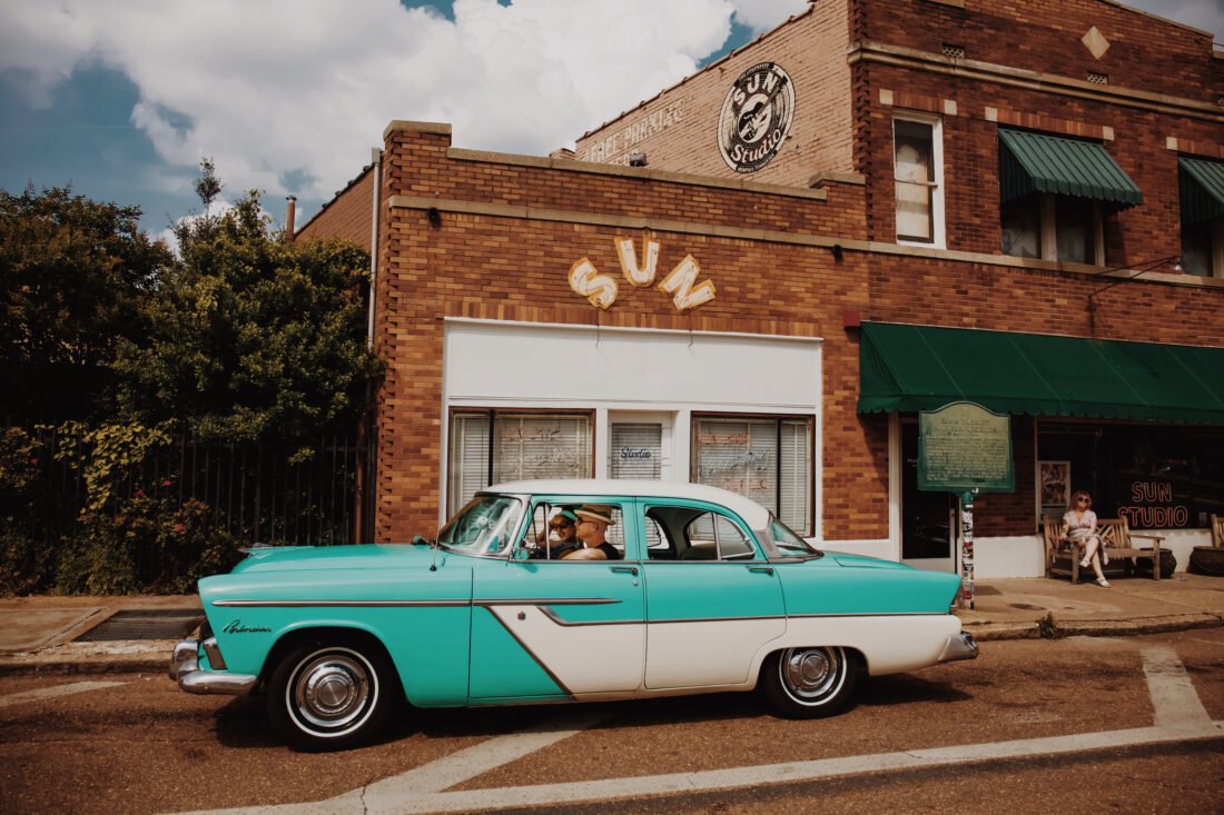 A vintage aqua car is parked outside a recording studio building