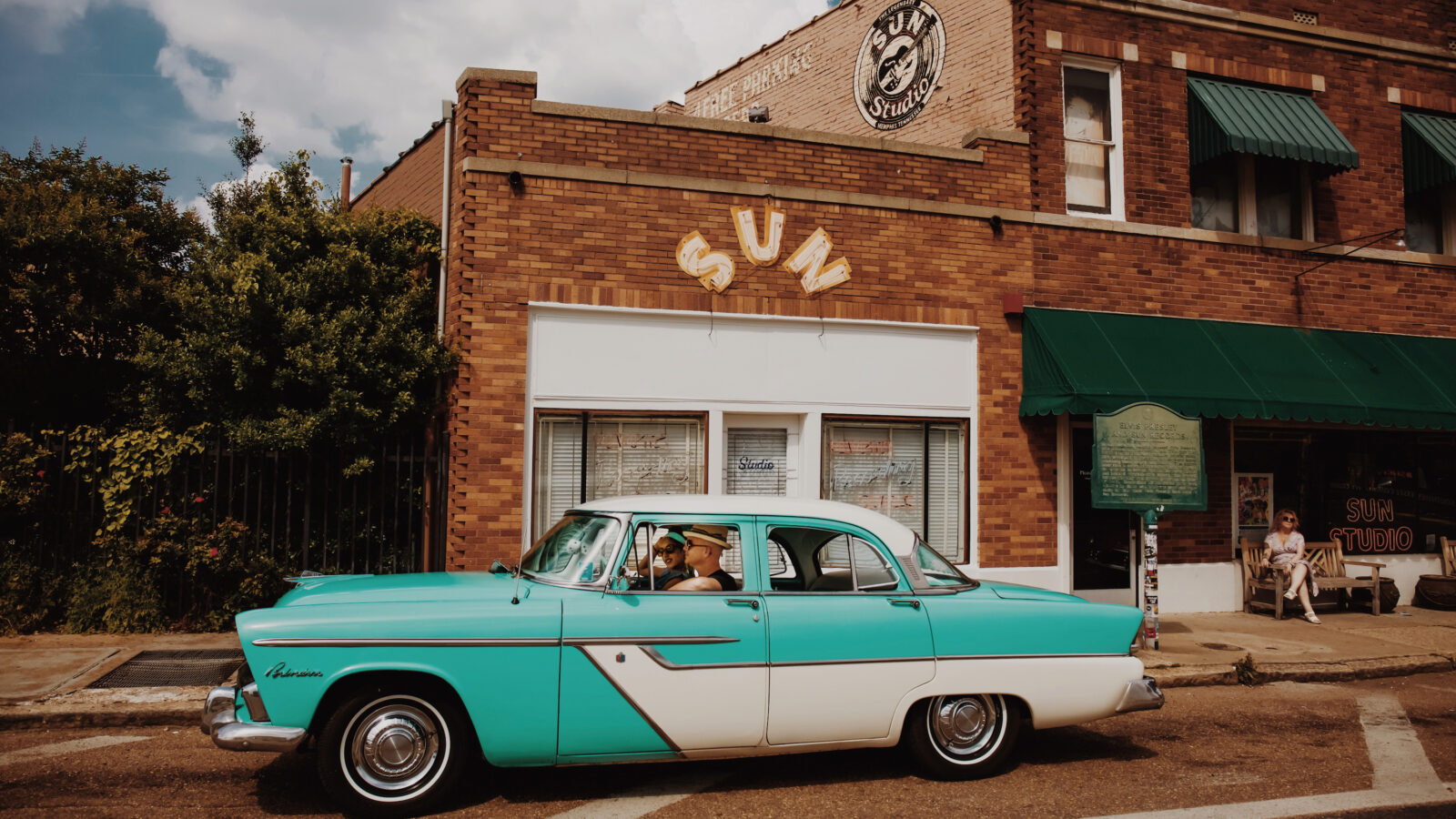 A vintage aqua car is parked outside a recording studio building