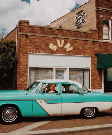 A vintage aqua car is parked outside a recording studio building