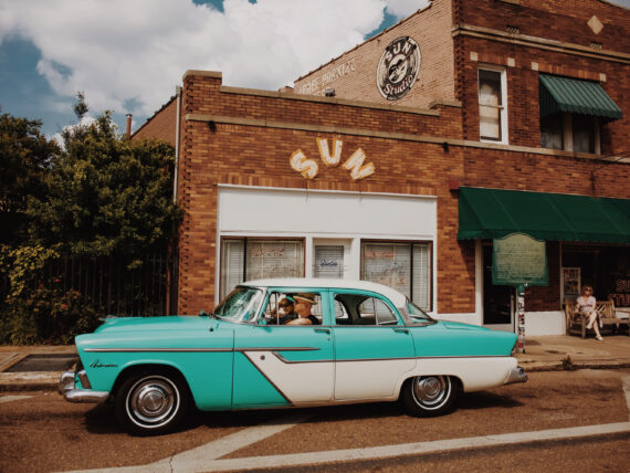 A vintage aqua car is parked outside a recording studio building