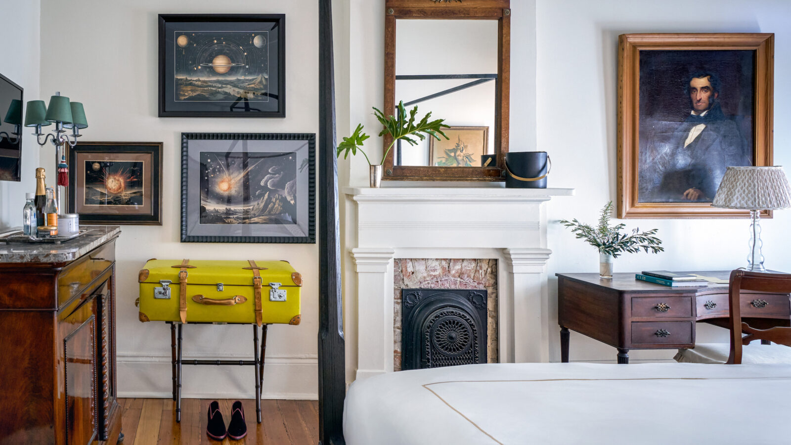Inside a hotel room with antique art, an ornate old fireplace, and a yellow suitcase