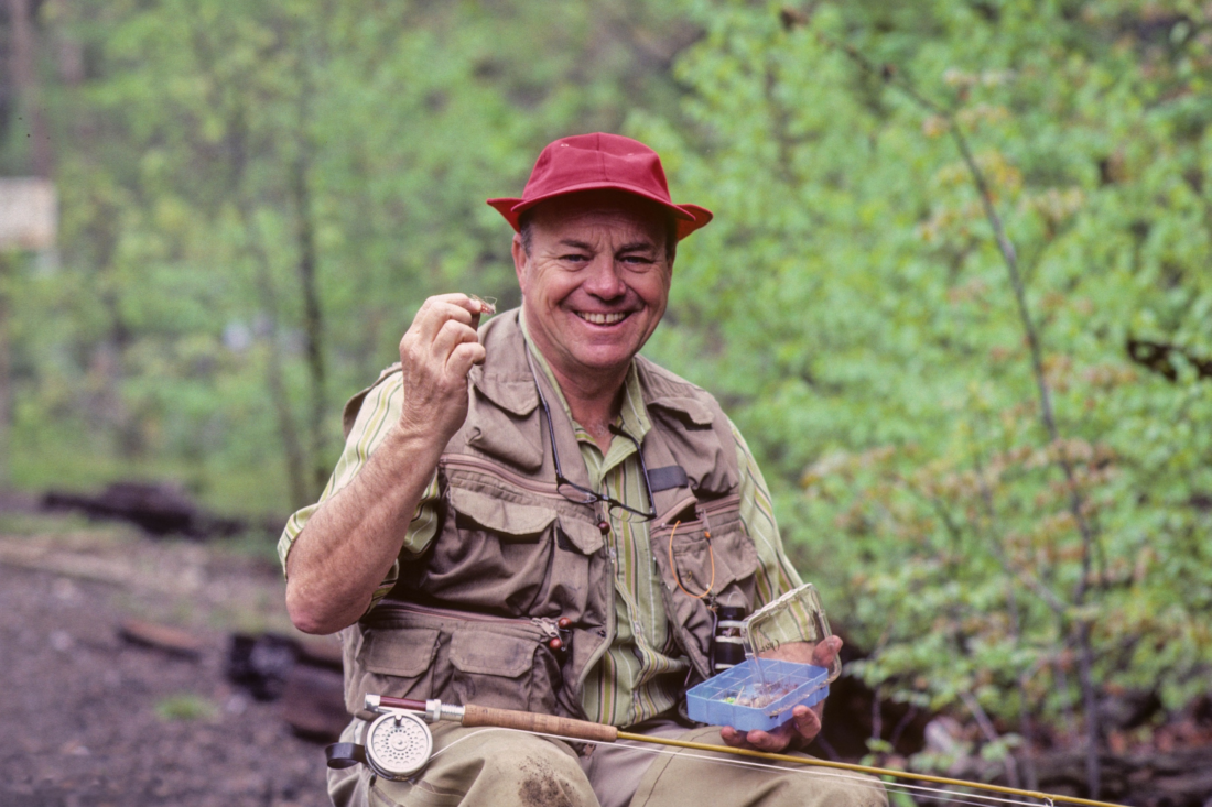 A man sitting in the woods with fly fishing supplies